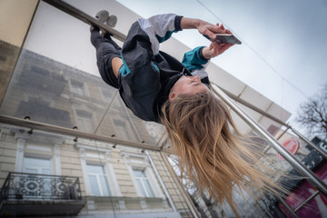 Girl hanging by feet upside down in the street and using smartphone. Concept of overusing social...