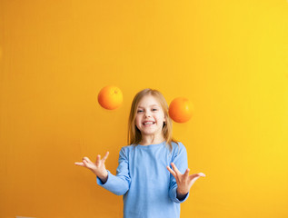 Cute baby 6-8 years old, baby girl blonde beauty on an orange background throws and catches fruits appelsinandand laughs,