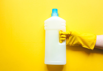 Hand in a yellow glove holding a  detergent of cleaning fluid on a yellow background.  Top view and space for  text. Flatlay and yellow on yellow