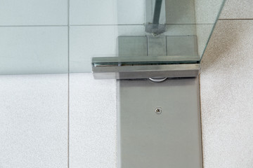 Glass door fittings, swivel mechanism holding the door metal loop on the tile floor close up detail.