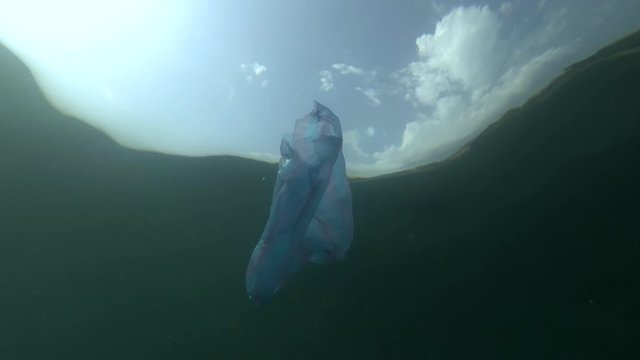 Plastic pollution, blue bag and school of Sand Smelt swims underwater on background blue sky with clouds. Low-angle shot. Plastic debris underwater. Plastic garbage environmental pollution problem 
