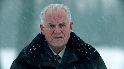 Elderly grandfather - gray-haired grandfather under the snowfall and looking in the camera