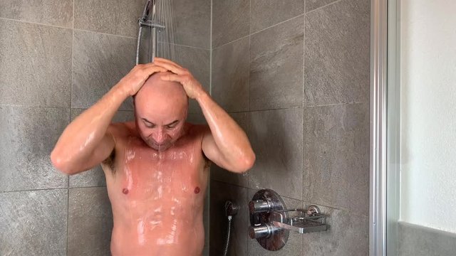 funny bald middle-aged man washes in the shower