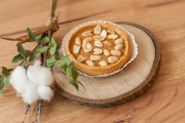 Obraz na płótnie Canvas A peanut cake on a natural wood stand on a rumbled wooden background. Decor of cotton and lavender flowers. Candy store, coffee shop. Soft focus