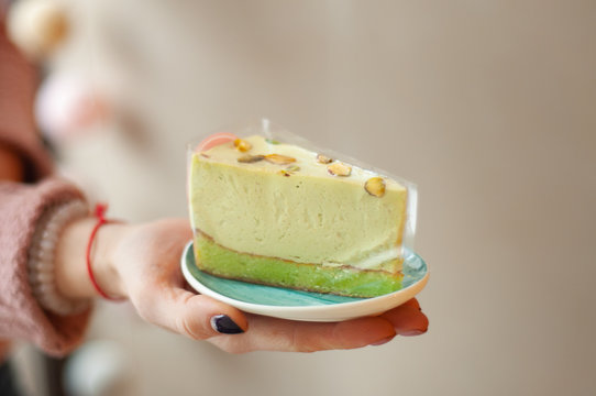 The girl holds a blue saucer with a piece of pistachios cake on her palm. Restaurant, coffee shop, pastry, bakery, sweets shop. Diet weight loss fitness. Healthy lifestyle. Gluten-free lactose. Amulet