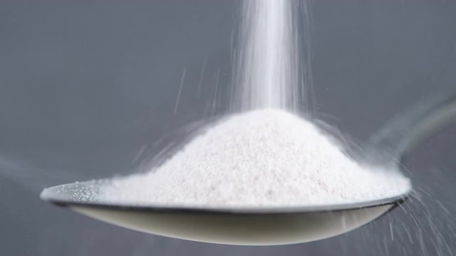 pouring collagen powder in black spoon. grey background closeup. Natural beauty and health supplement