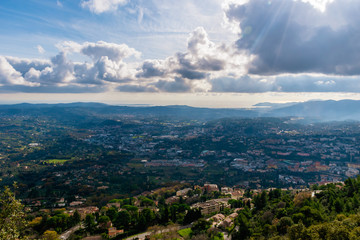 The panoramic view of a medieval French town in Côte d'Azur under the cloudy sky and the Meditarrenean sea coastline in the horizon