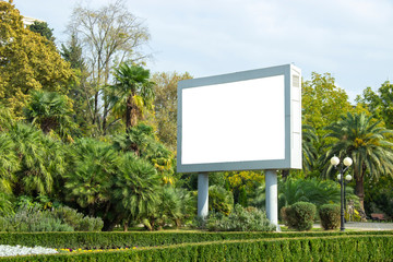 Blank street billboard poster in the park on the background of tropical plants. information banner, copy space for text.