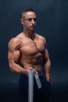 Muscular man doing calisthenic exercise with power band isolated on the black background