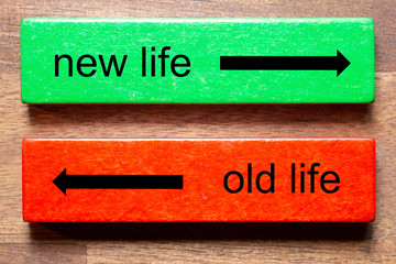 new life is written on a green block and old life is the text on a red block. The background is a dark wood background.
