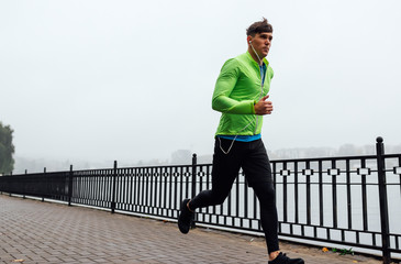 Horizontal image of young athelte man running in the morning on the fog lake background. Fitness...