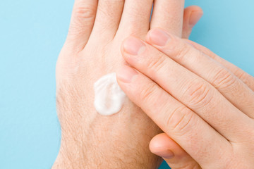 Young man hands using moisturizing white cream on light blue table background. Pastel color....
