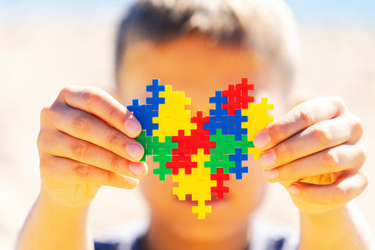 World autism awareness day concept. Boy holding colorful puzzle heart in front of his face