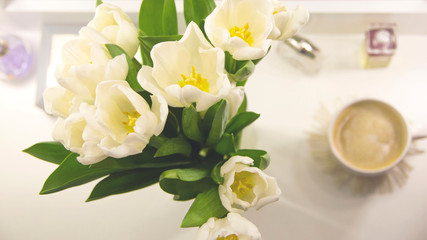 A cup of coffee in the morning next to a bouquet of white tulips. Spring holiday card.