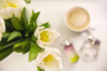 White tulips on the table next to a cup of morning coffee in a bright cozy home atmosphere. Congratulations on March 8 and Mother's Day.