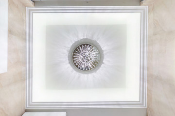 looking up on suspended ceiling with halogen spots lamps and drywall construction in empty room in apartment or house. Stretch ceiling white and complex shape.