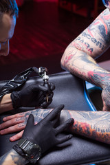 man artist tattoos in studio beats tattoos. Unusual male profession. An informal punk rocker clogs a sleeve arm. Sterile gloved procedure. Ink device tattoo machine. self-expression individuality