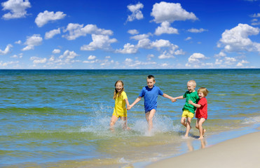 Two girls and two boys in colorful t-shirts running on a sandy beach