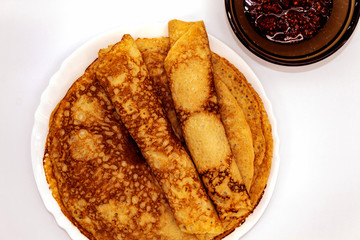 Raspberry jam and a plate of fresh fried pancakes on a light background