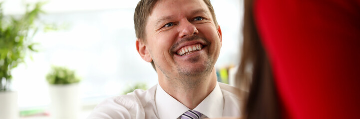 Young smiling businessman sitting and making agreement by handshake with colleague