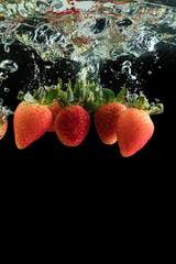 Fresh red strawberries under water on a black background. Splash of water from falling berries.