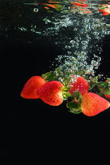 Fresh red strawberries under water on a black background. Splash of water from falling berries.