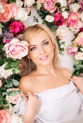 Beautiful romantic young blonde woman with natural makeup posing against a background of flowers, flower wall in pink. Perfume and cosmetic concept