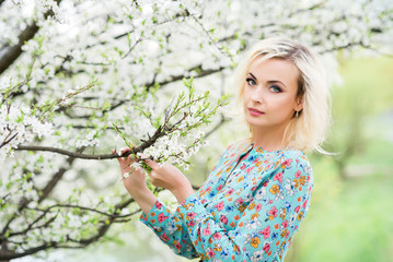 Romantic beautiful woman in a Park on the lake stands against a background of a flowering tree. Spring photo with a beautiful girl in a floral dress