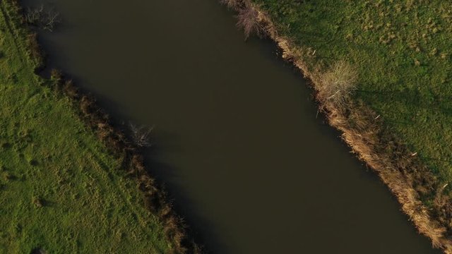 Aerial - Video that goes from a birds eye of view above a meandering river to a normal view showing an agricultural landscape in europe