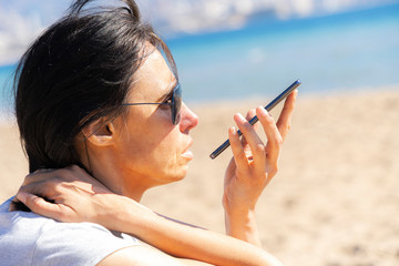 Woman using a smart phone voice recognition function, recording voice message sitting on the beach near sea