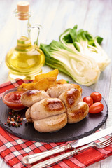 Grilled sausages, bratwurst with tomato sauce, spices and herbs on a stone plate, rustic background