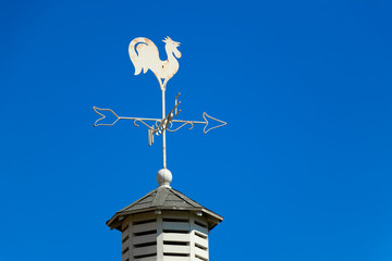 White rooster weather vane show the wind direction on blue sky background