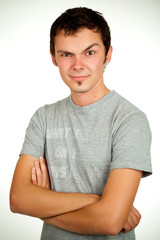 Fototapeta premium Portrait of a Caucasian young positive guy in a gray shirt and jeans posing on a gray background. Concept of a successful young student or novice employee. Advertising space