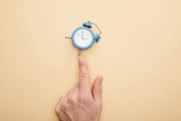 cropped view of man touching small alarm clock on beige background