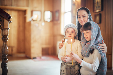 Russian woman praying in front of icons on her knees with her little daughters in the Orthodox...