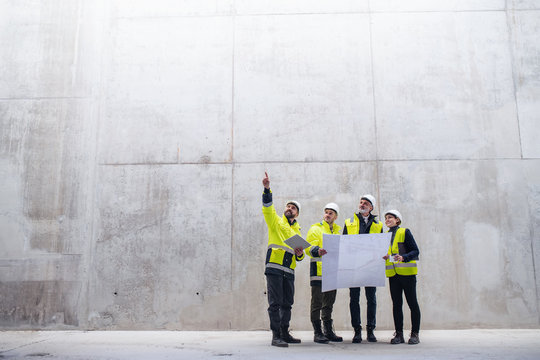 A group of engineers standing against concrete wall on construction site.