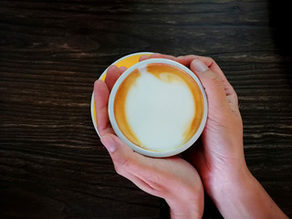 Close up of hand holding a Capucino coffee drinks yellow cup on wooden table backgrounds above