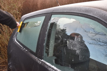 Frosty morning, ice cover window car, bad weather conditions, scraping ice from the car windows by hand with an ice scraper early in the morning