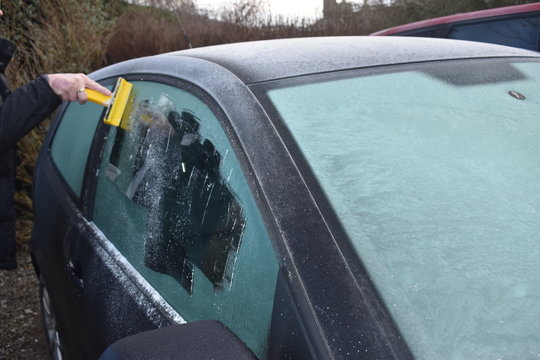 Frosty morning, ice cover window car, bad weather conditions, scraping ice from the car windows by hand with an ice scraper early in the morning