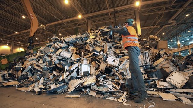 Recycling factory worker sorts garbage into a pile.