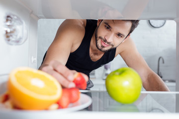 selective focus of handsome man taking strawberry from plate in fridge