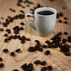 cup of black coffee on a wooden board with a beautiful grain and substituted coffee beans, with limited depth of field