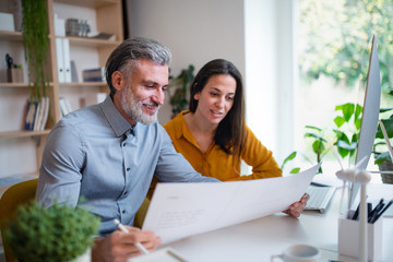 Architects sitting at the desk indoors in office, looking at blueprints.