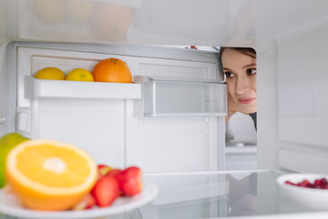selective focus of girl looking at fruits in fridge