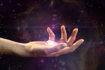 Female hand with light coming from the palm, against the background of the galaxy. The concept of...