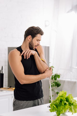 selective focus of surprised man measuring muscle on hand in kitchen