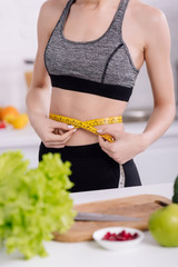 cropped view of sportive girl measuring waist near fresh food in kitchen