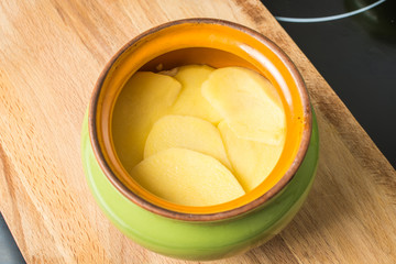 Sliced fresh potatoes lay in ceramic pot for cooking in oven.