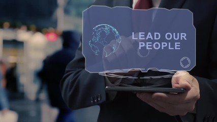 Unrecognizable businessman uses hologram on smartphone with text Lead our people. Man in shirt and jacket with holographic screen on background of entrance to the airport or train station