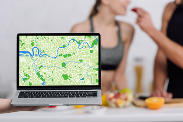selective focus of laptop with online map near couple in kitchen